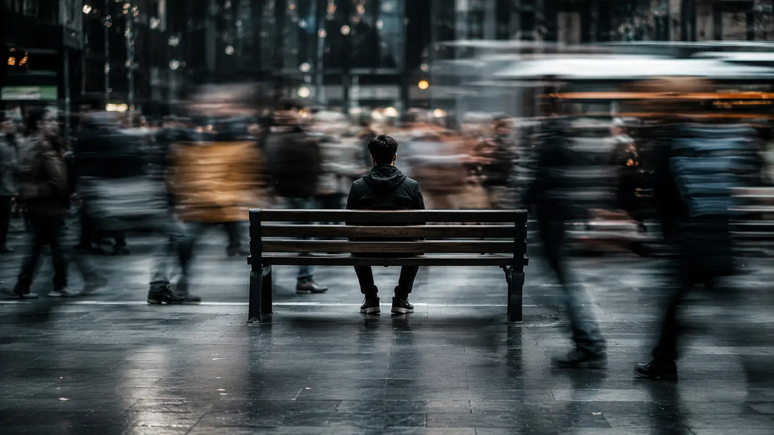 A person sitting perfectly still on a city bench while all pedestrians around them are motion-blurred in movement, the person the only sharp and stationary element in the frame