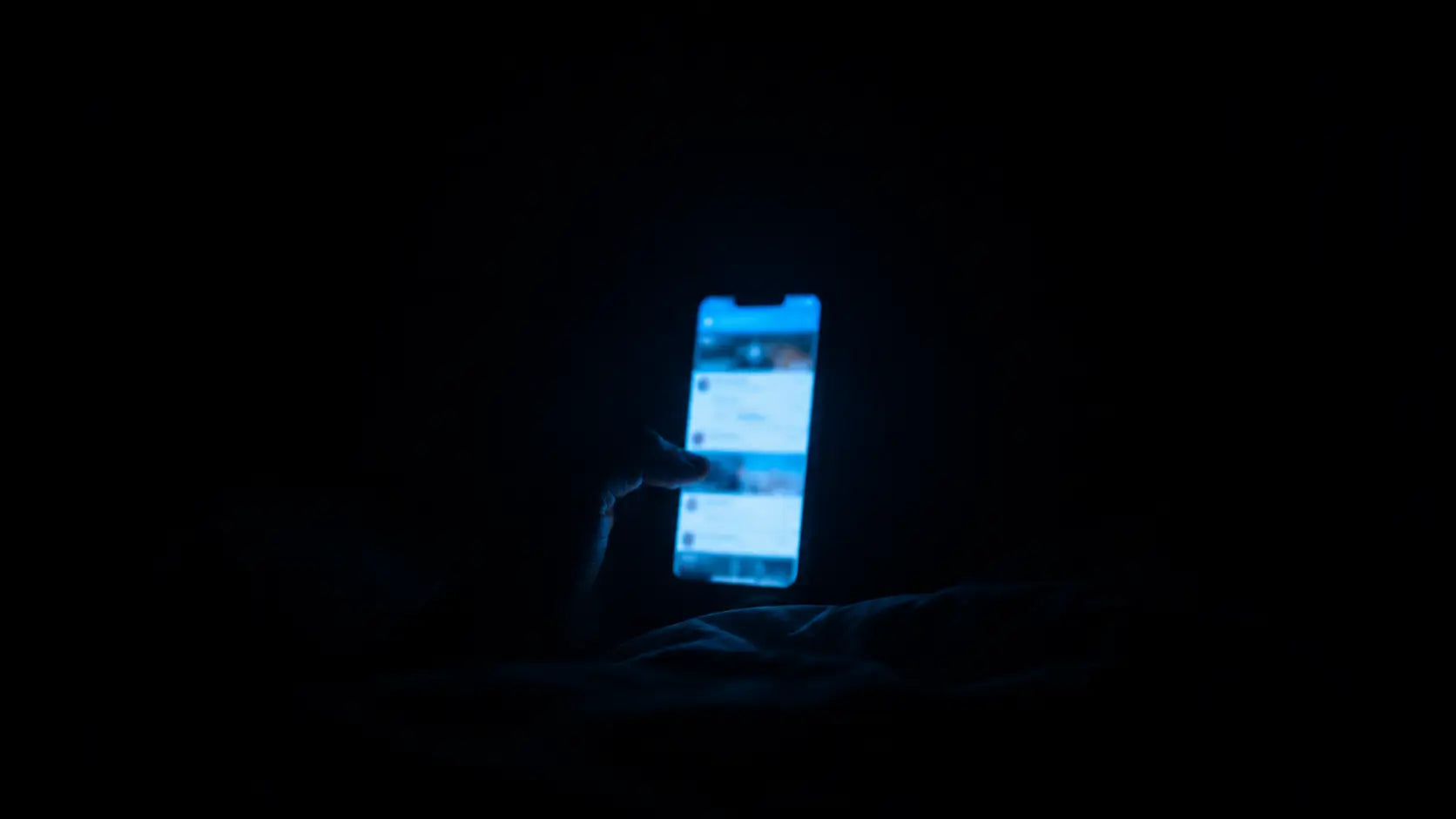 A phone screen casting blue light in a completely dark bedroom with a blurred social media feed visible, the glow the only illumination in the room, symbolising the doomscrolling loop